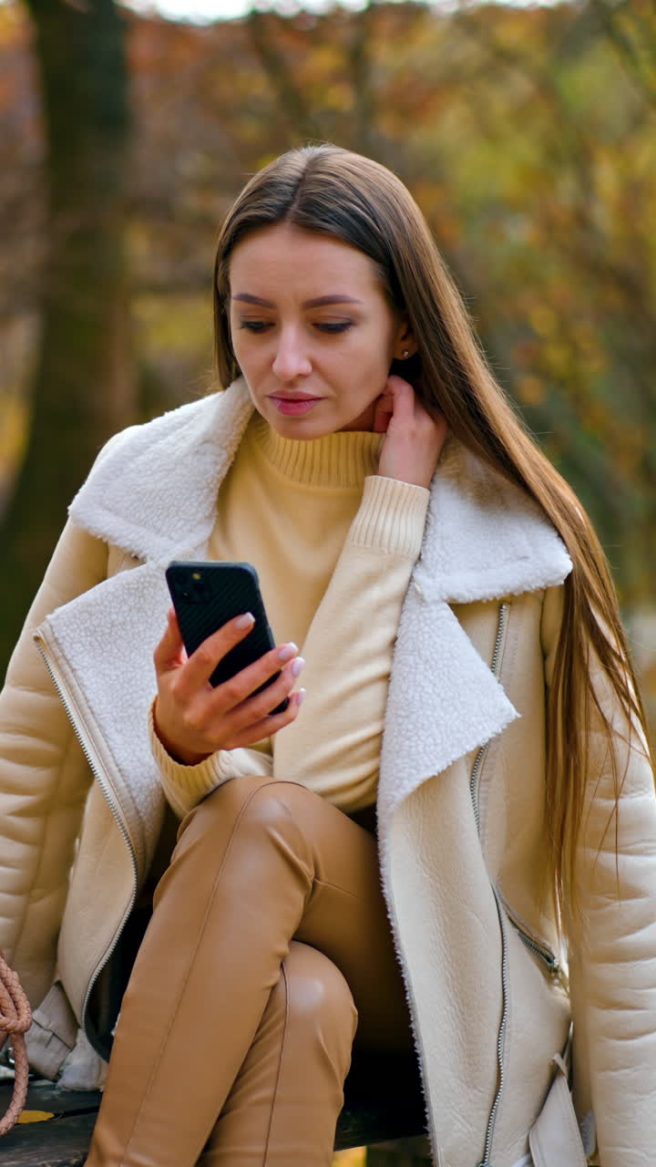 Serious pensive woman looking at her phone focused. Lady is smiling slightly as the camera approaches. Nature autumn backdrop in blur. Vertical video