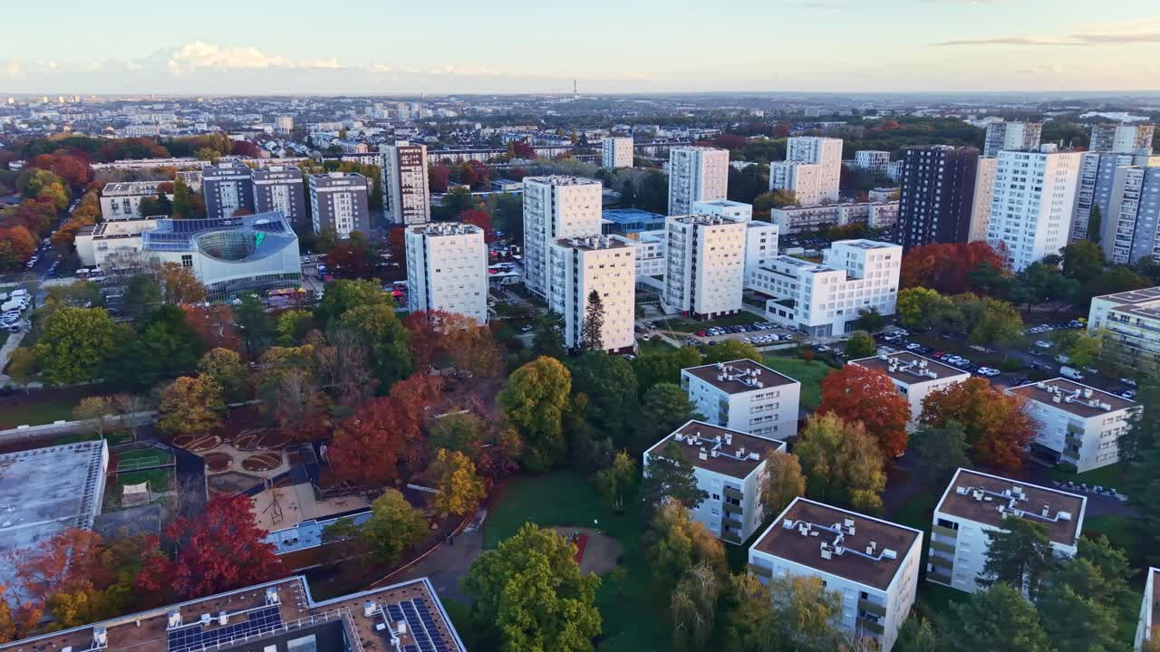 Lateral drone shot over Le Blosne district in Rennes showing Jean-Normand Square, the conservatory, residential buildings and autumn trees at sunrise