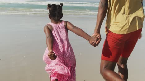 african american father and daughter holding hands running on the beach