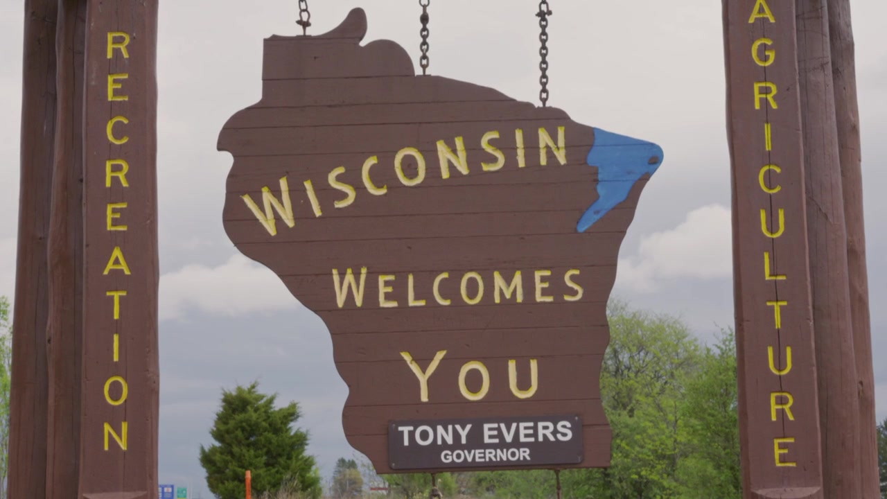 Ripresa cinematografica con gimbal, inclinazione verso il basso, del cartello "Wisconsin vi dà il benvenuto" con movimento di telecamera fluido e stabilizzato verso il basso all'aperto
