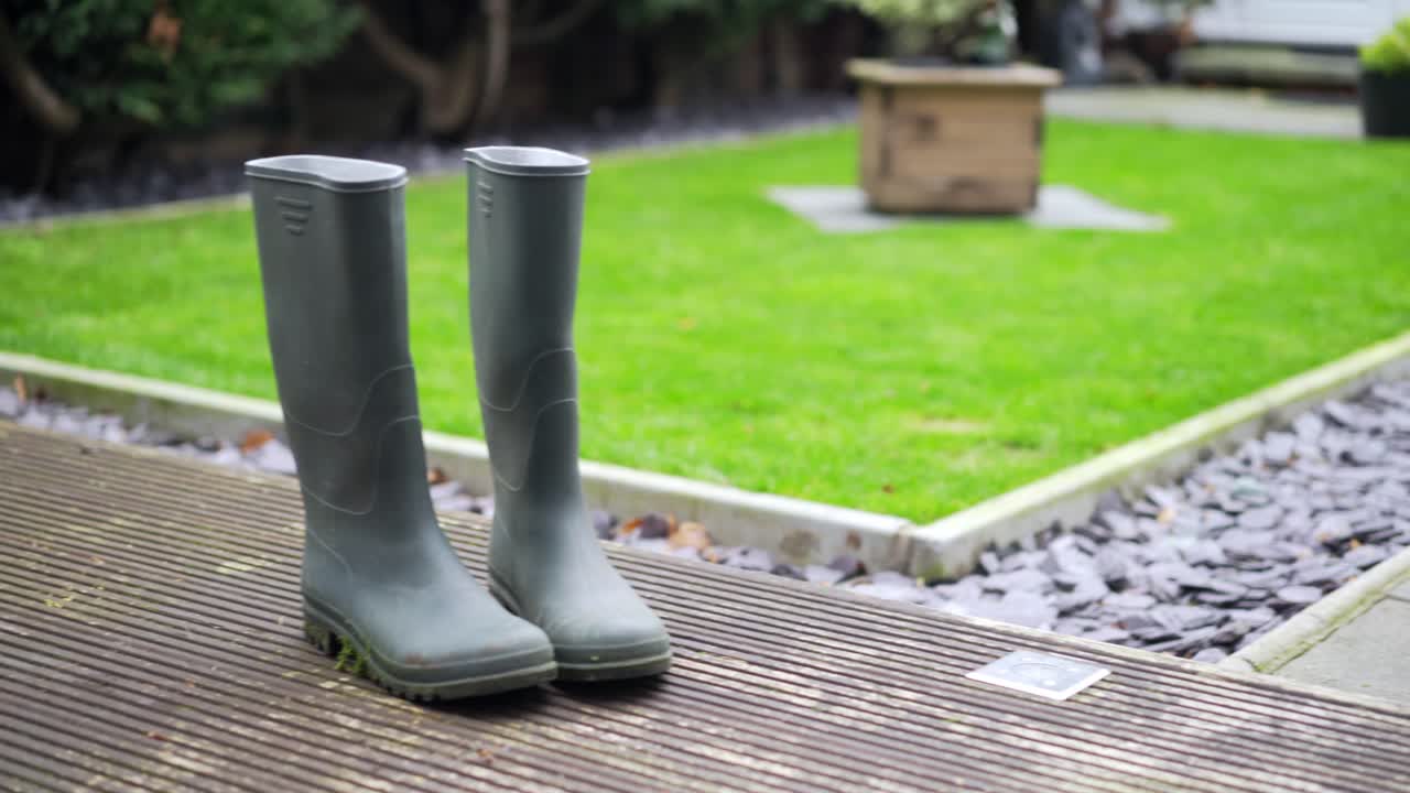 Green wellington boots on decking with grass in background pan right to left