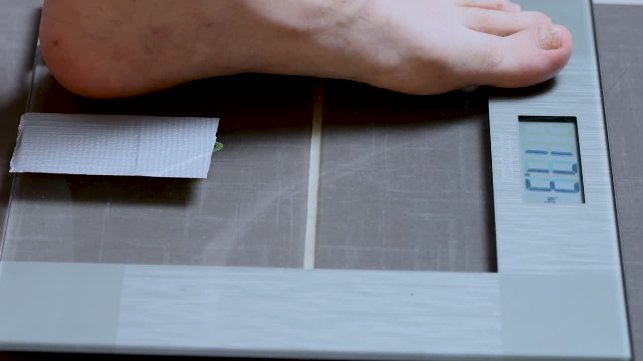 남자가 가정용 저울에 올라 자신의 체중을 확인하고 뒤로 물러납니다.