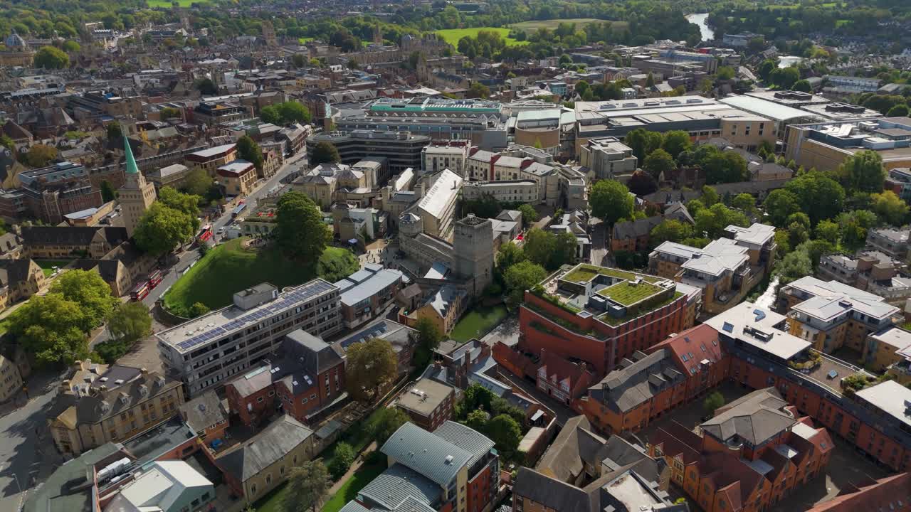 Drone pulls back and ascends from Oxford Castle and Prison, revealing Oxford’s skyline with historic spires, modern green rooftop architecture, and a blend of ancient and contemporary city landmarks