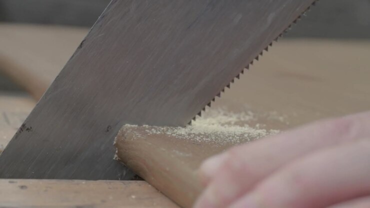 Mano di operaio che usa una sega a mano per segare un pezzo di legno