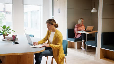 two millennial female creatives working at laptop computers in an office