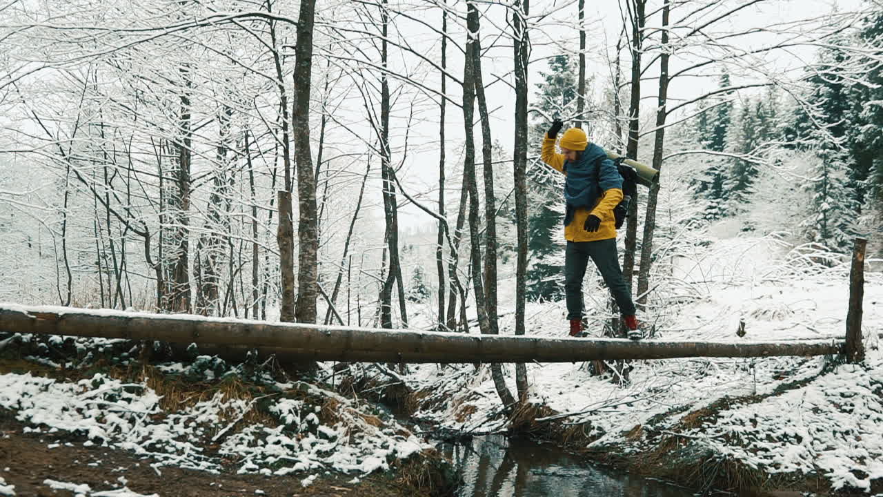 Um alpinista atravessando um riacho em um tronco em uma floresta nevada