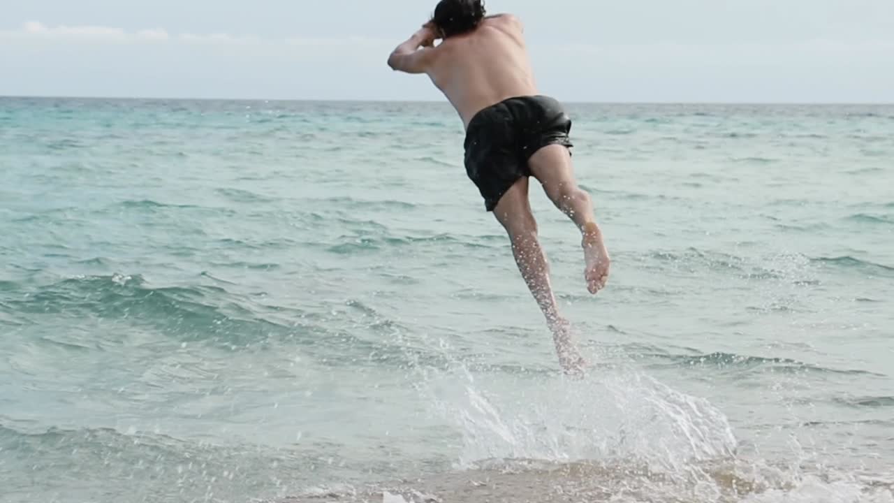 A man comes to the beach running and jumps into the water doing a dive. Then he goes out shaking his hair