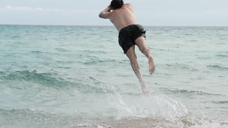 a man comes to the beach running and jumps into the water doing a dive. then he goes out shaking his hair