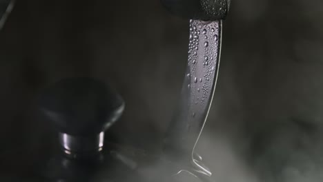 Condensation-drips-on-tea-kettle-handle-as-steam-vapor-rises,-close-up