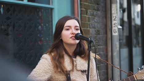 female musician busking playing acoustic guitar and singing to crowd outdoors in street