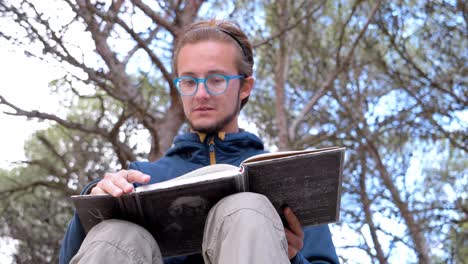 Slow-motion-low-angle-shot-of-a-man-reading-an-Albert-Einstein-book-in-the-forest