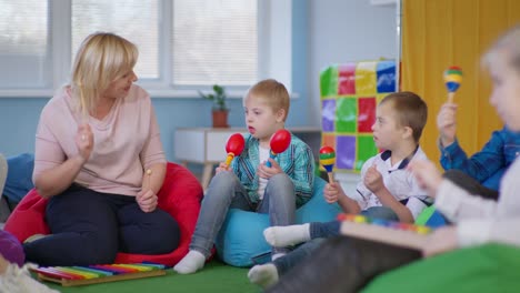 boys with down syndrome listen attentively to music female teacher, children with musical instruments sit on multicolored bean bag chairs