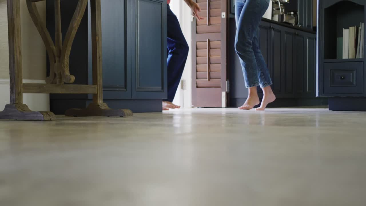 Low section of biracial couple spending time at home holding dancing barefoot