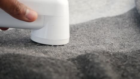 removing lint from gray sweater with handheld lint remover