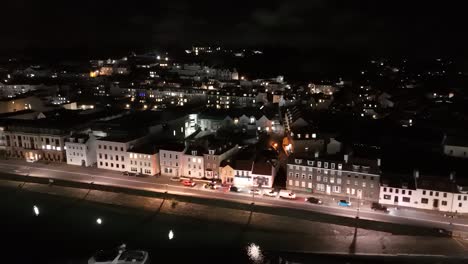 Vuelo-De-Drones-Por-La-Noche-A-Lo-Largo-De-La-Explanada-Glategny-De-St-Peter-Port-Guernsey-Hacia-La-Avenida-De-San-Julián-Con-La-Ciudad-Al-Fondo-Y-El-Elizabeth-College-Iluminado