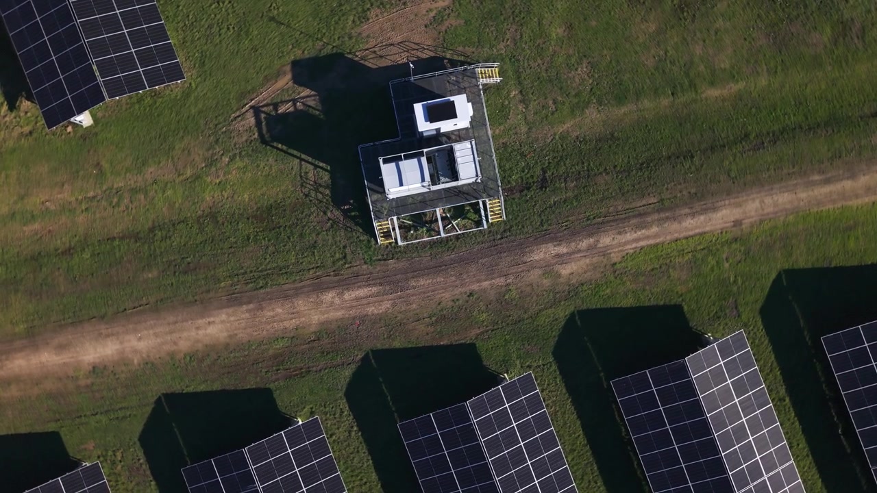 Dronevideo av pene rader med solcellepaneler og en teknisk innhegning i The Basin, Melbourne. Klart dagslys, skarpe skygger, levende grønt gress og rike detaljer skaper en energigivende, miljøvennlig scene.