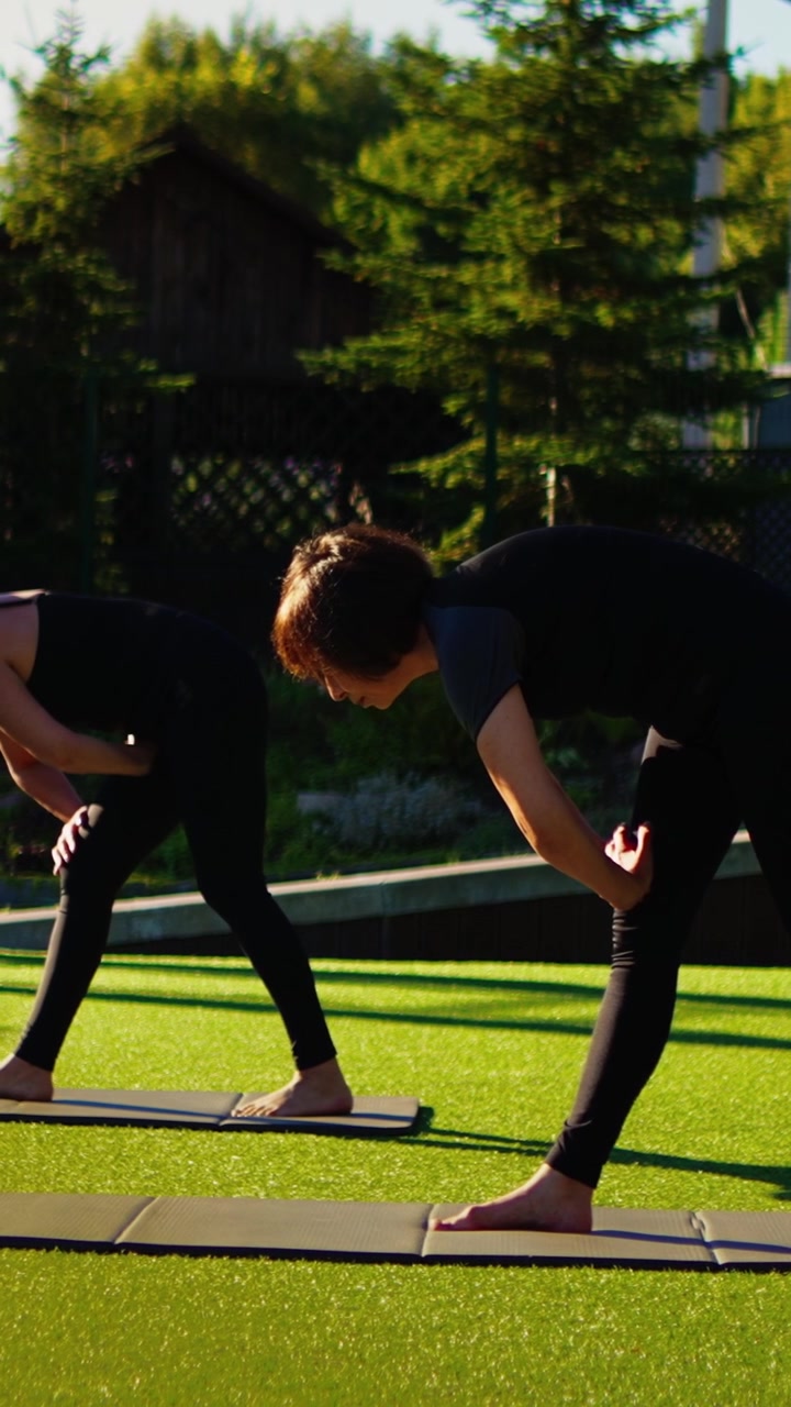 Women Practicing Yoga Stretching Exercises Outdoors on Green Grass