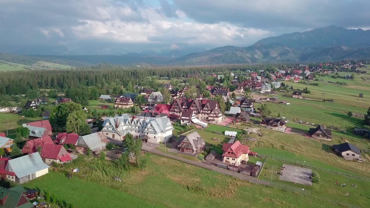 Aerial shot of a small mountain village in the close range to the majestic Tatra Mountains. Camera slightly rotates and pulls out.