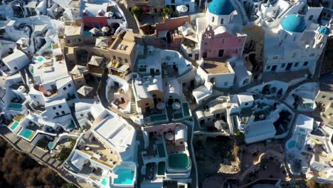 Vista-Aérea-De-Arriba-Hacia-Abajo-De-Oia-Con-Casas-Cueva-Blancas-Y-Villas-Que-Revelan-Un-Estilo-De-Vida-De-Lujo-En-Santorini,-Grecia