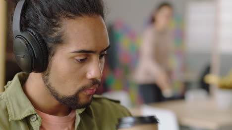 cerca joven hombre de raza mixta usando computadora portátil navegando mensajes en línea compartiendo comunicación de red estudiante bebiendo café disfrutando escuchando música en una oficina moderna