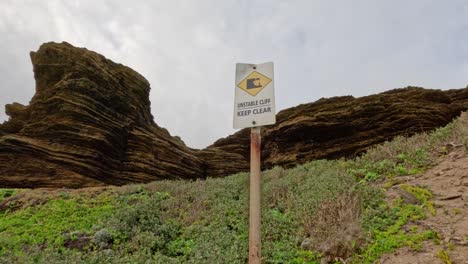 caution sign near unstable limestone cliffs and greenery