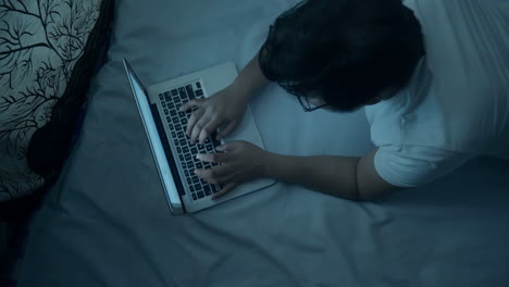 top view of an indian man lying on bed and using laptop computer at night