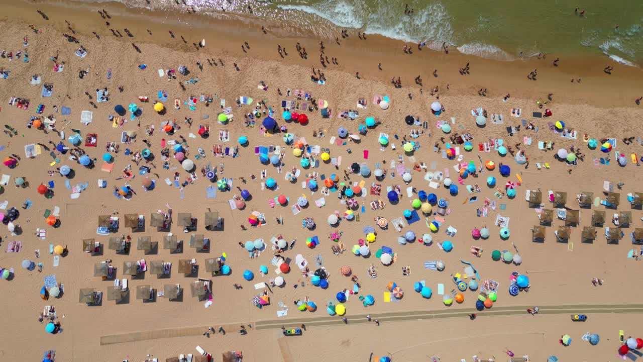 View from above and from the side, the beautiful Guincho beach full of people with parasols adding color to the beach and waves breaking on the seashore,Cascais,Portugal