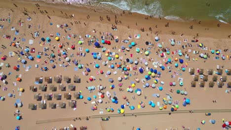 view from above and from the side, the beautiful guincho beach full of people with parasols adding color to the beach and waves breaking on the seashore,cascais,portugal