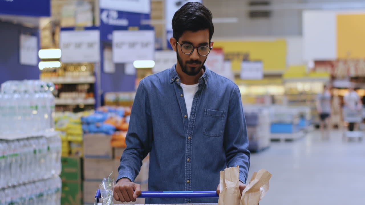 Portrait Of A Tall Boy With Glasses Leaning On The Shopping Cart In The Supermarket Looking Straight At The Camera And Smiling