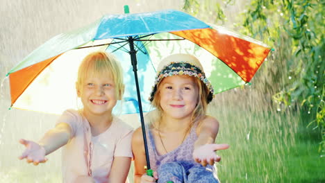Zwei-Sorglose-Mädchen-Sitzen-Unter-Einem-Regenschirm,-Der-Sich-Vor-Dem-Warmen-Sommerregen-Versteckt-422-Zeitlupe-10-B