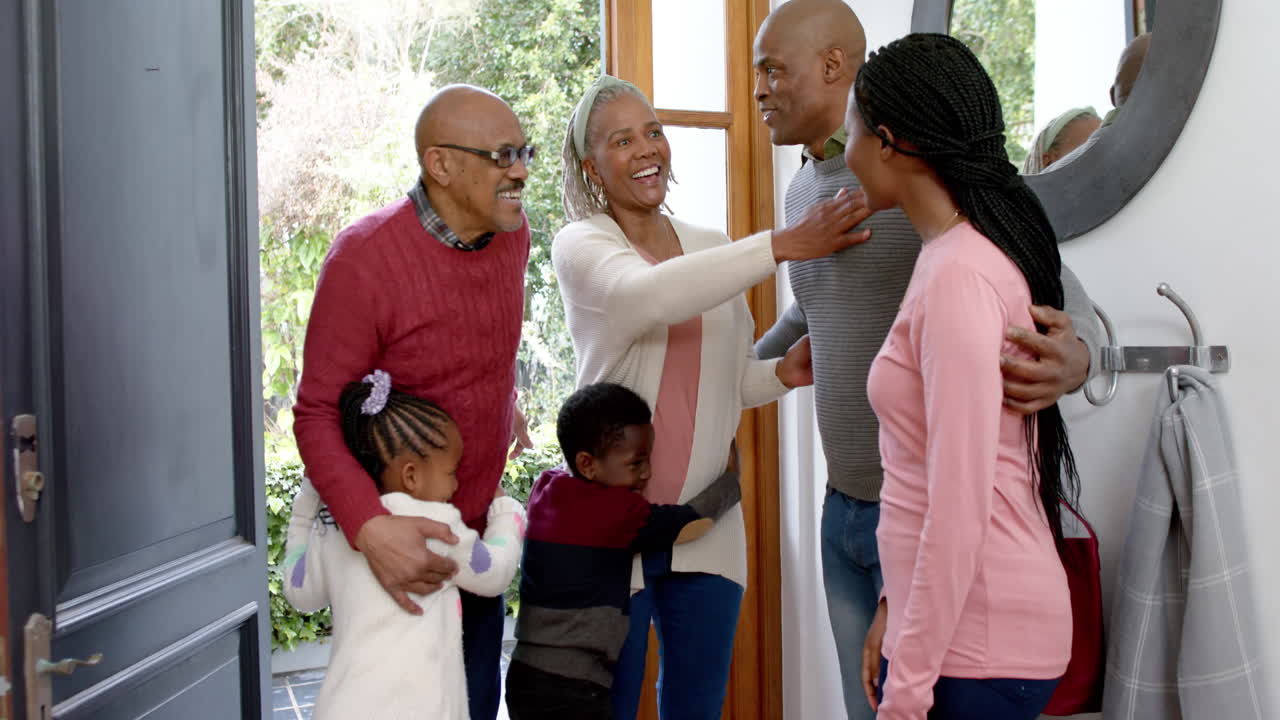 Happy african american parents, son and daughter welcoming visiting grandparents, slow motion