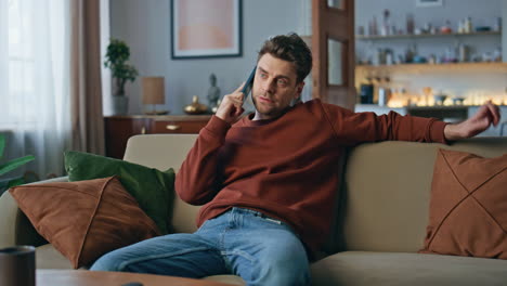 bored guy calling cellphone relaxing at couch. serious man talking smartphone