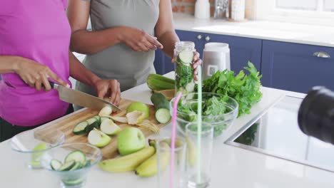 Feliz-Madre-E-Hija-Afroamericana-Preparando-Bebidas-Saludables,-Haciendo-Videos-Usando-Cámara