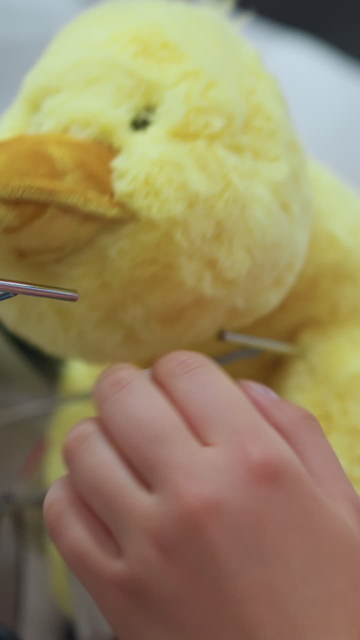 분홍색 옷을 입은 여자가 다른 은 동물들로 둘러싸인 상점 선반에 있는 노란색 플러시 장난감을 부드럽게 만지며, 장난감은 흐릿한 빛의 효과를 가지고 있으며, 그녀는 그것을 조심스럽게 검사합니다.