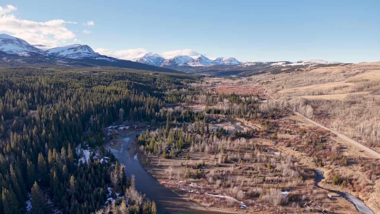 Flygfotografi med drönare av en vidsträckt torr prärie i Montana med sparsamt gräs och en remsa av vintergrön skog som leder mot avlägsna snötäckta berg under en klar himmel.