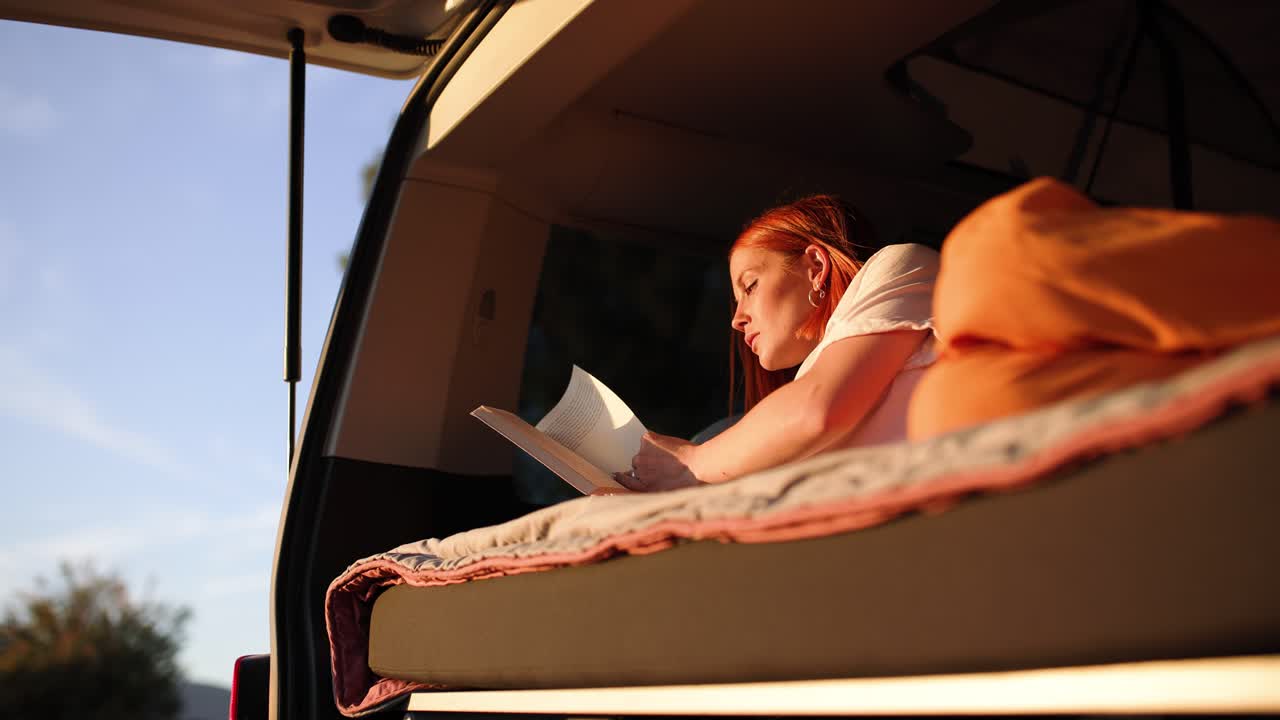 Giovane donna che legge un libro in camper al tramonto