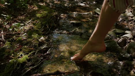 man carefully stepping barefoot into cold natural small creek close up