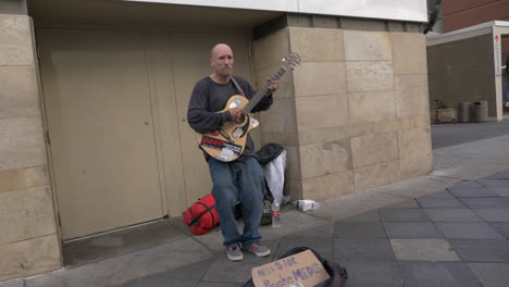 homeless man playing guitar in need of donations for his psychiatric medication in downtown denver colorado