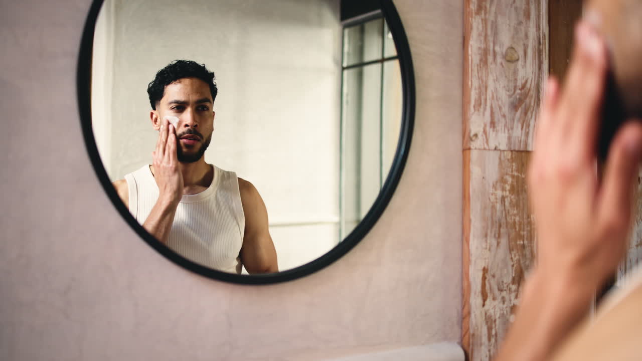 Giovane uomo che applica crema viso allo specchio del bagno