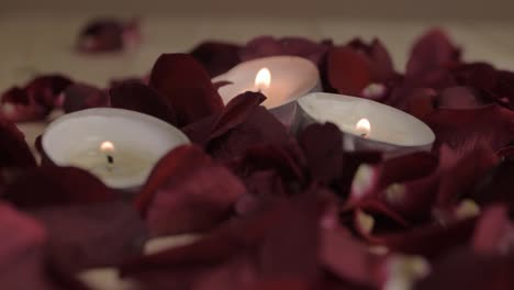 velas de té encendidas sobre un lecho de pétalos de rosas rojas