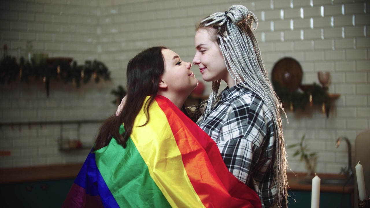 Young lesbian women covered with lgbt flag rub their noses and being cute