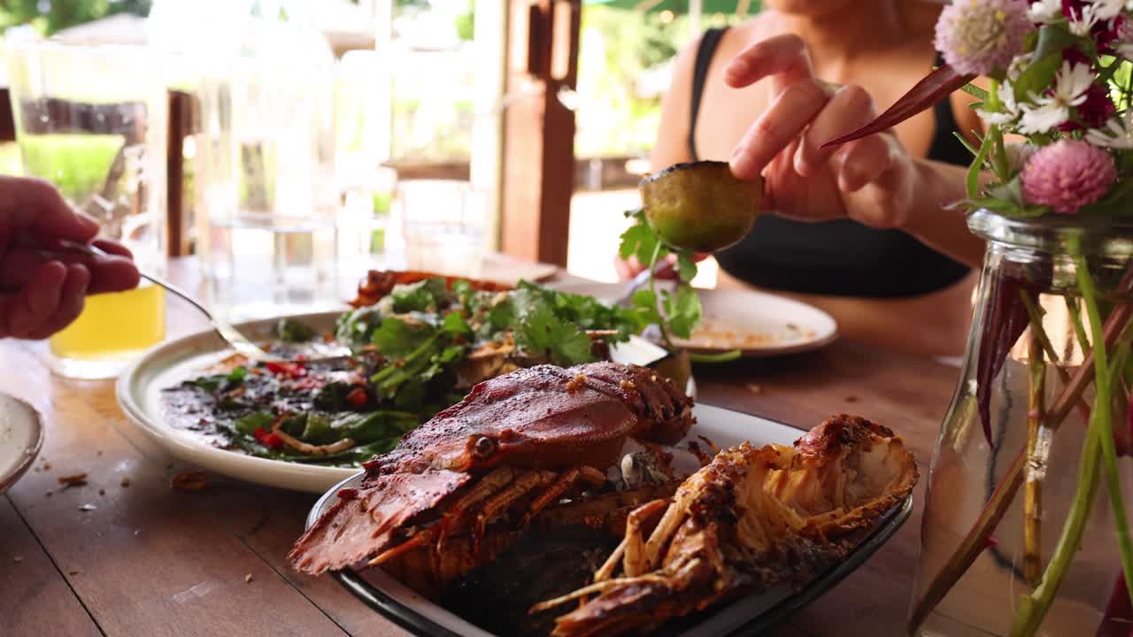 A person enjoys grilled mantis shrimp with fresh greens in a sunlit restaurant setting