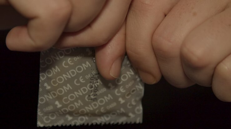 Mani che aprono la confezione di un preservativo e rivelano un nuovo preservativo