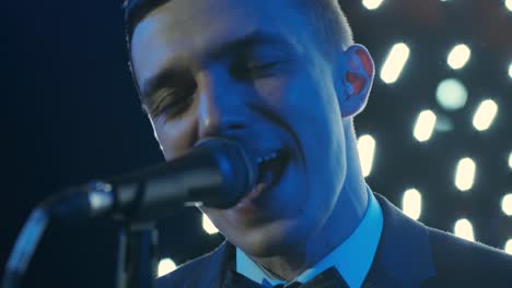 man singing song in microphone during performance on stage on rock concert. close up man rock star singer on music concert on colorful light background