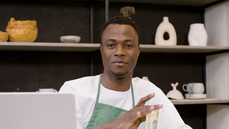 confident male small business owner holding money and looking at camera in the pottery shop