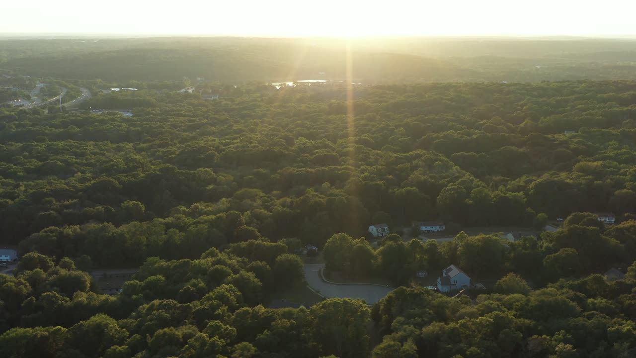 trucking shot in the bright summer sunset over a forested rural area of the Northeastern USA, with intense lens flare