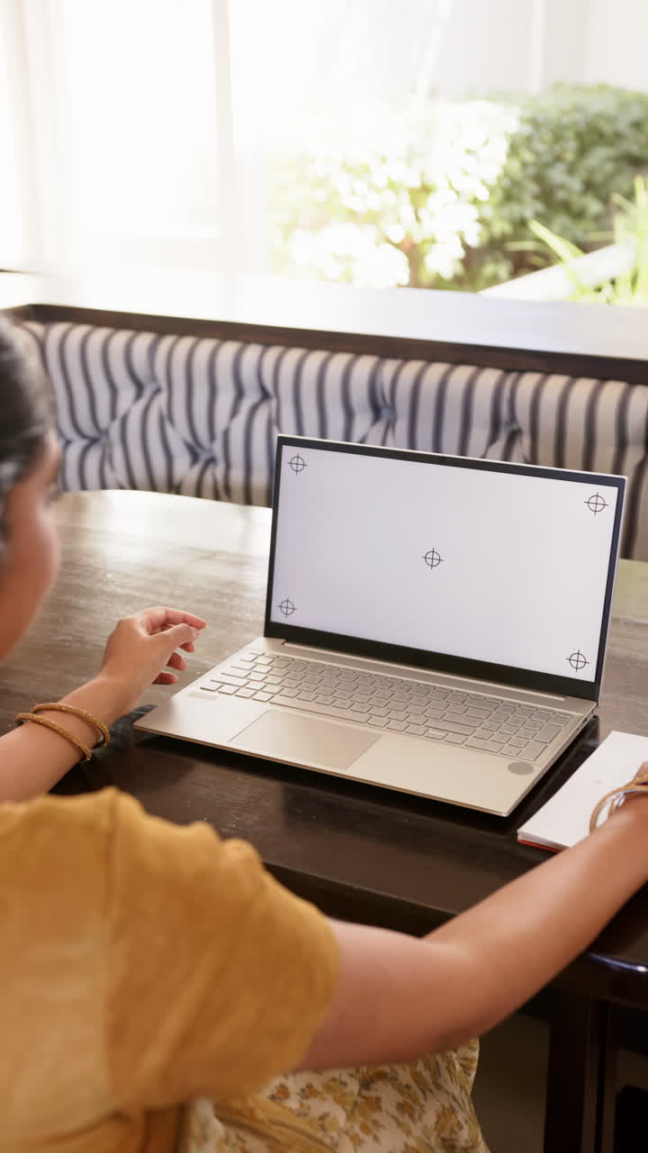 Vertical video: Using laptop, woman working from home at table with notebook