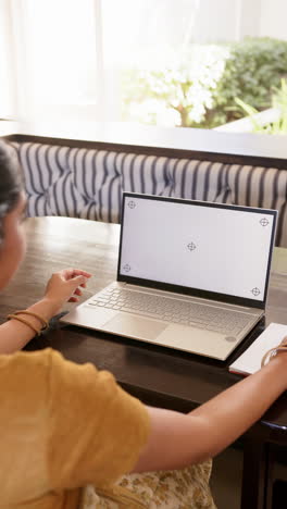vertical video: using laptop, woman working from home at table with notebook