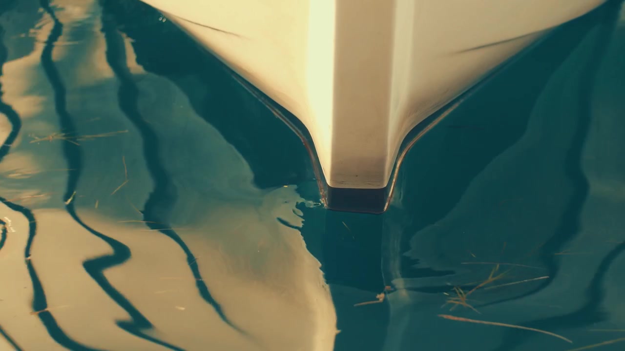 Cinematisk vintage abstrakt optagelse af blide havbølger, der skaber forvrængede, kunstneriske refleksioner af en hvid bådforstavn på vandoverfladen.