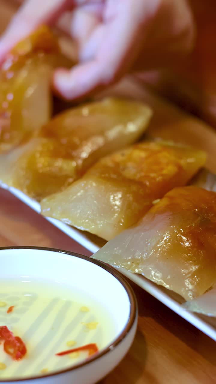 Close-up shot of hands picking up translucent shrimp dumplings served with chili dipping sauce